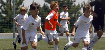 Kids wearing Real Madrid uniforms running during a soccer drill on an outdoor field.