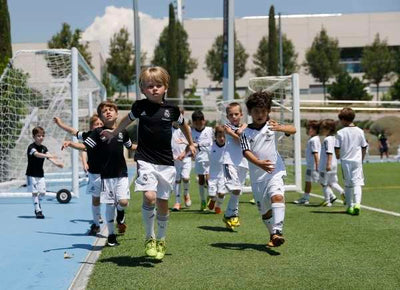 Children playing soccer on a sports field with goalposts in the background.
